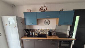 A compact kitchen with a white refrigerator, a microwave, a toaster, and a sink. There are cabinets with blue handles and a decorative ship model on the wall. - Little house with pool 4 people (Payzac)