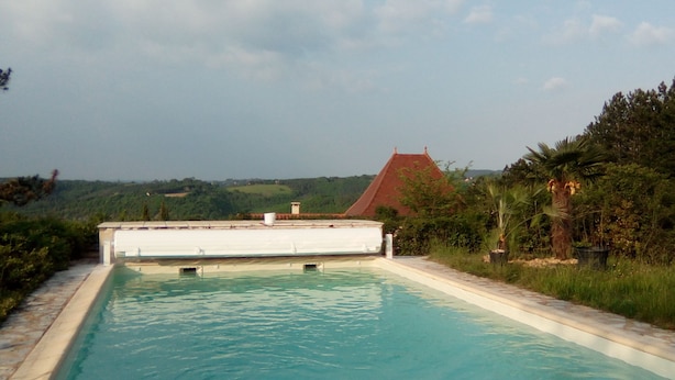 Ein Schwimmbecken mit freiem Blick auf die umliegende Landschaft, darunter ein Gebäude mit rotem Dach und üppiges Grün.