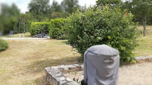 Ein Gartenbereich mit einer Steinmauer, einer überdachten Sitzgelegenheit und einem Weg.