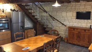 Una cocina rústica con una mesa de comedor de madera, sillas, un refrigerador y un televisor montado en la pared.