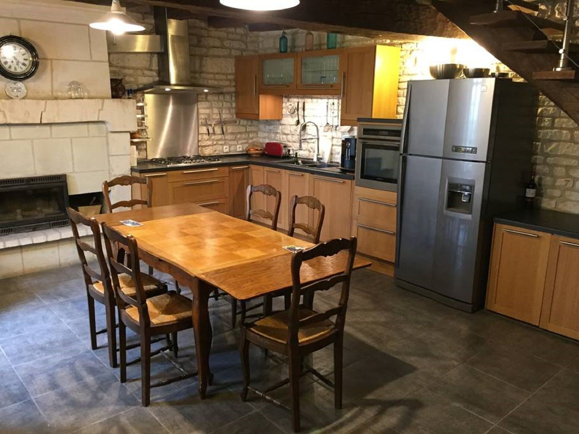 Une cuisine avec une table et des chaises en bois, un poêle, un réfrigérateur et un mur en pierre.