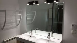 Un baño con lavamanos doble, un espejo grande y un perchero para toallas.