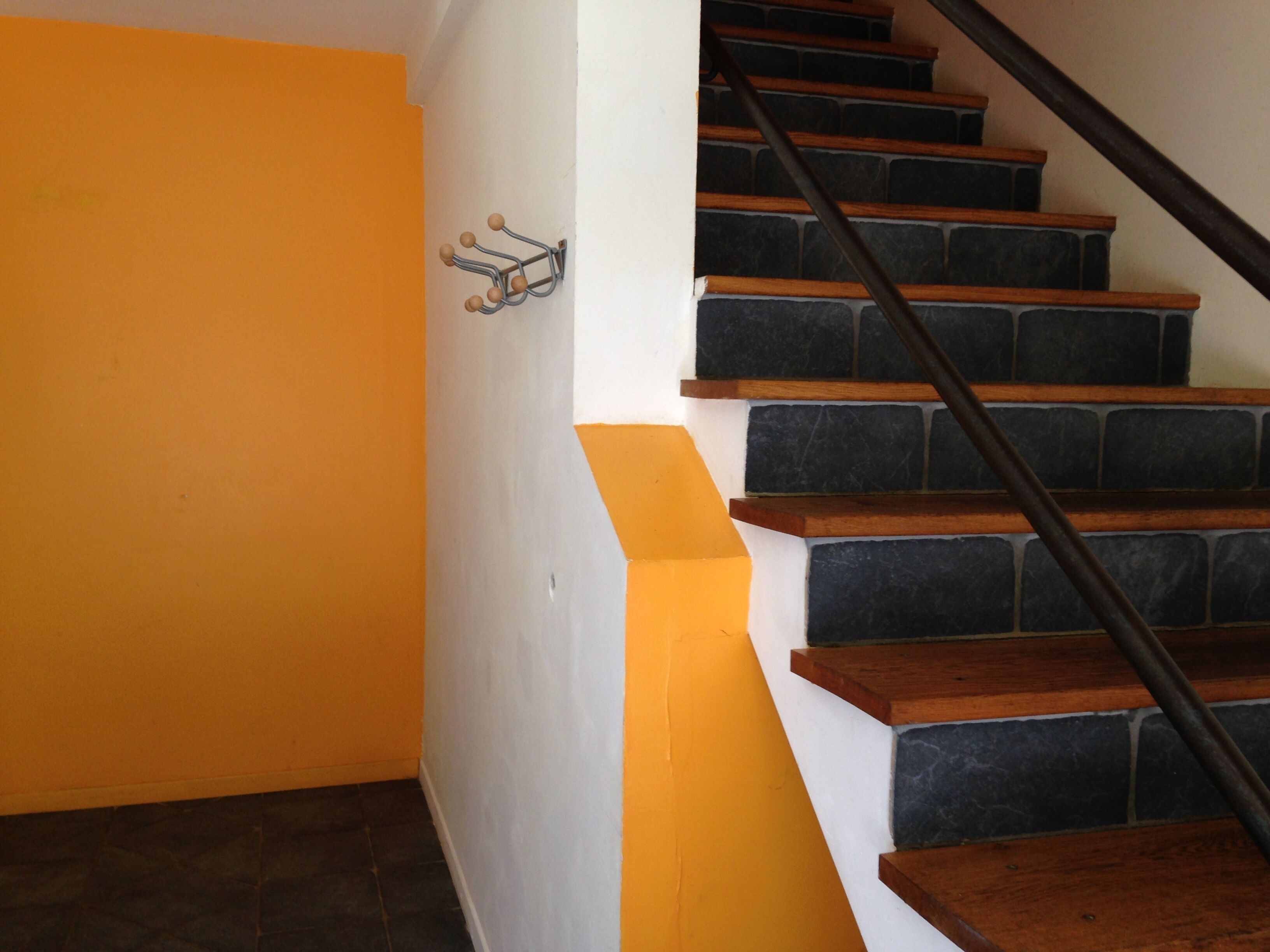 Eine Treppe mit dunklen Steinstufen und Holzhandläufen, die zu einer Zwischenebene mit einem Metall-Kleiderständer führt.