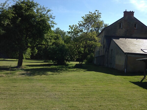 A large, rustic building with a sloped roof and a chimney, surrounded by a grassy field and trees.