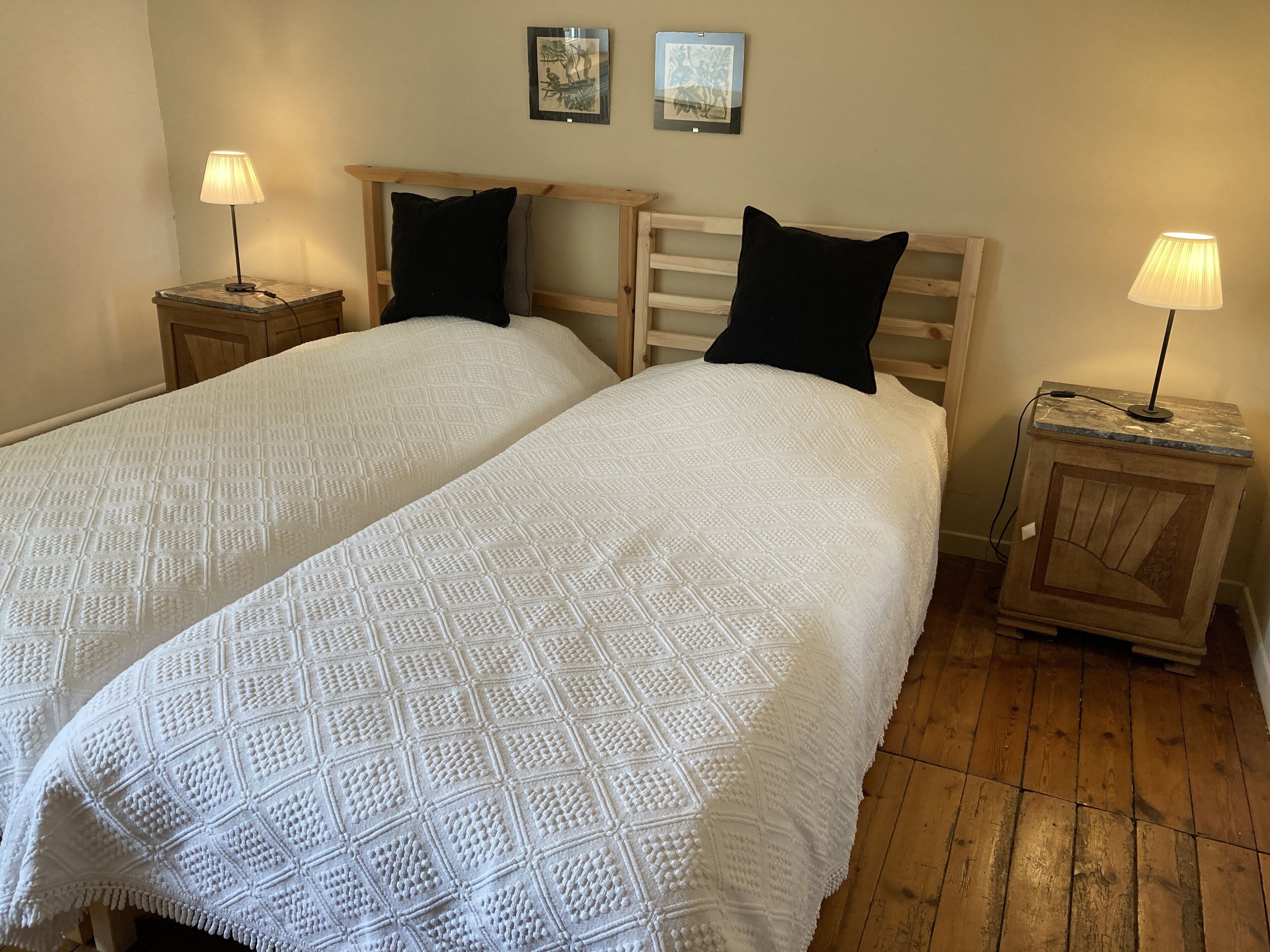 Uma cama de casal com colcha branca texturizada e duas almofadas pretas, ladeada por mesas de cabeceira de madeira com abajures.