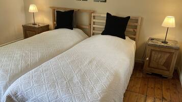 Uma cama de casal com colcha branca texturizada e duas almofadas pretas, ladeada por mesas de cabeceira de madeira com abajures.