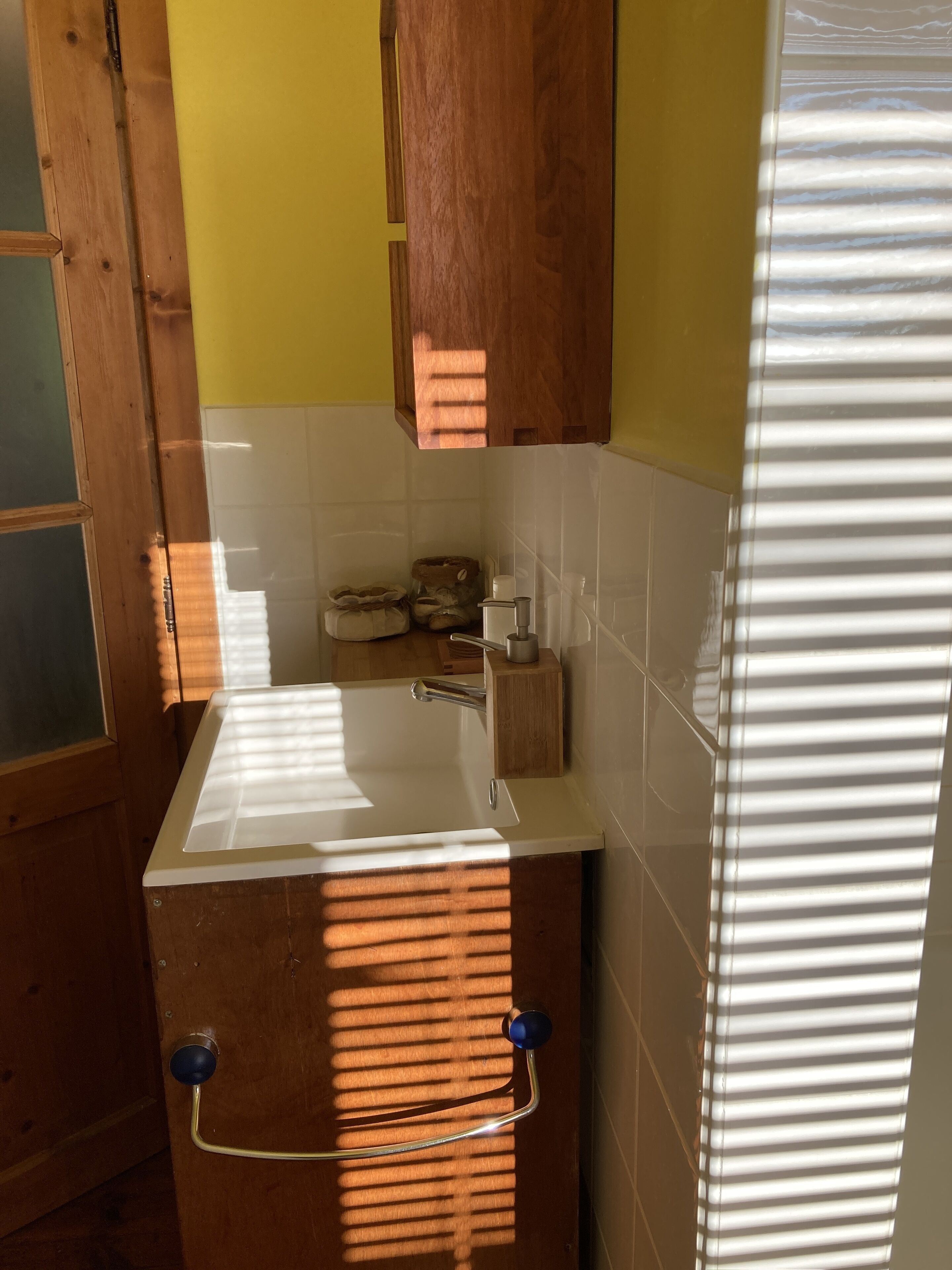 A kitchen with a white sink, wooden cabinets, and a window with blinds.