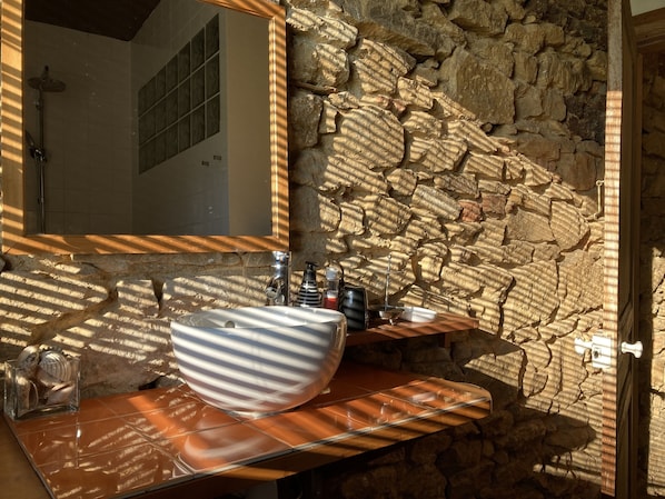 A bathroom with a stone wall, a large mirror, a white sink, and a wooden vanity.