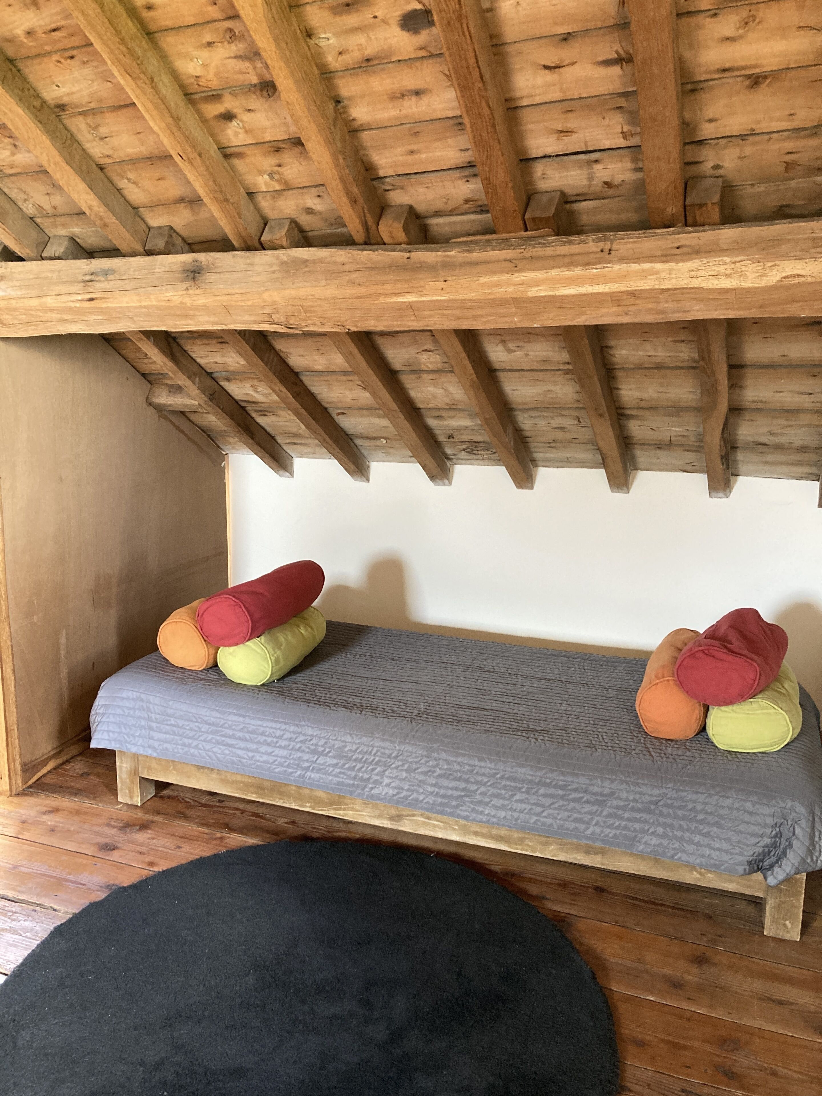 Eine Holzbank mit grauem Kissen und bunten Kissen.