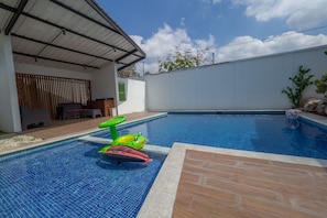 A swimming pool with a tiled edge, a covered seating area, and a white wall in the background.