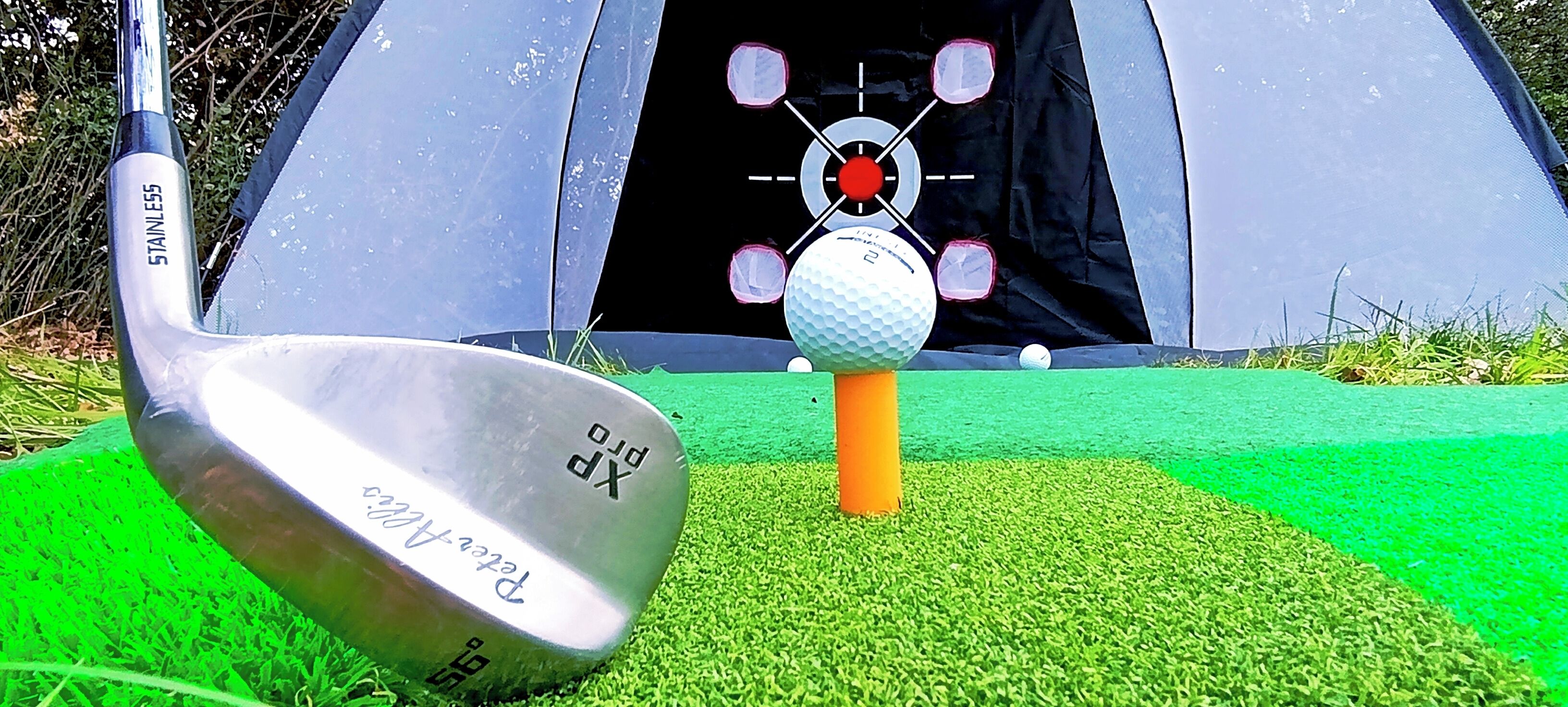 Un palo de golf y una pelota sobre césped artificial, con una tienda de campaña al fondo.