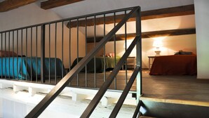 A room with a wooden staircase, a bed with a blue cover, and a table with a lamp. - Le 7 Mas - Suite Angélique & Adrienne (Saint-Andiol)