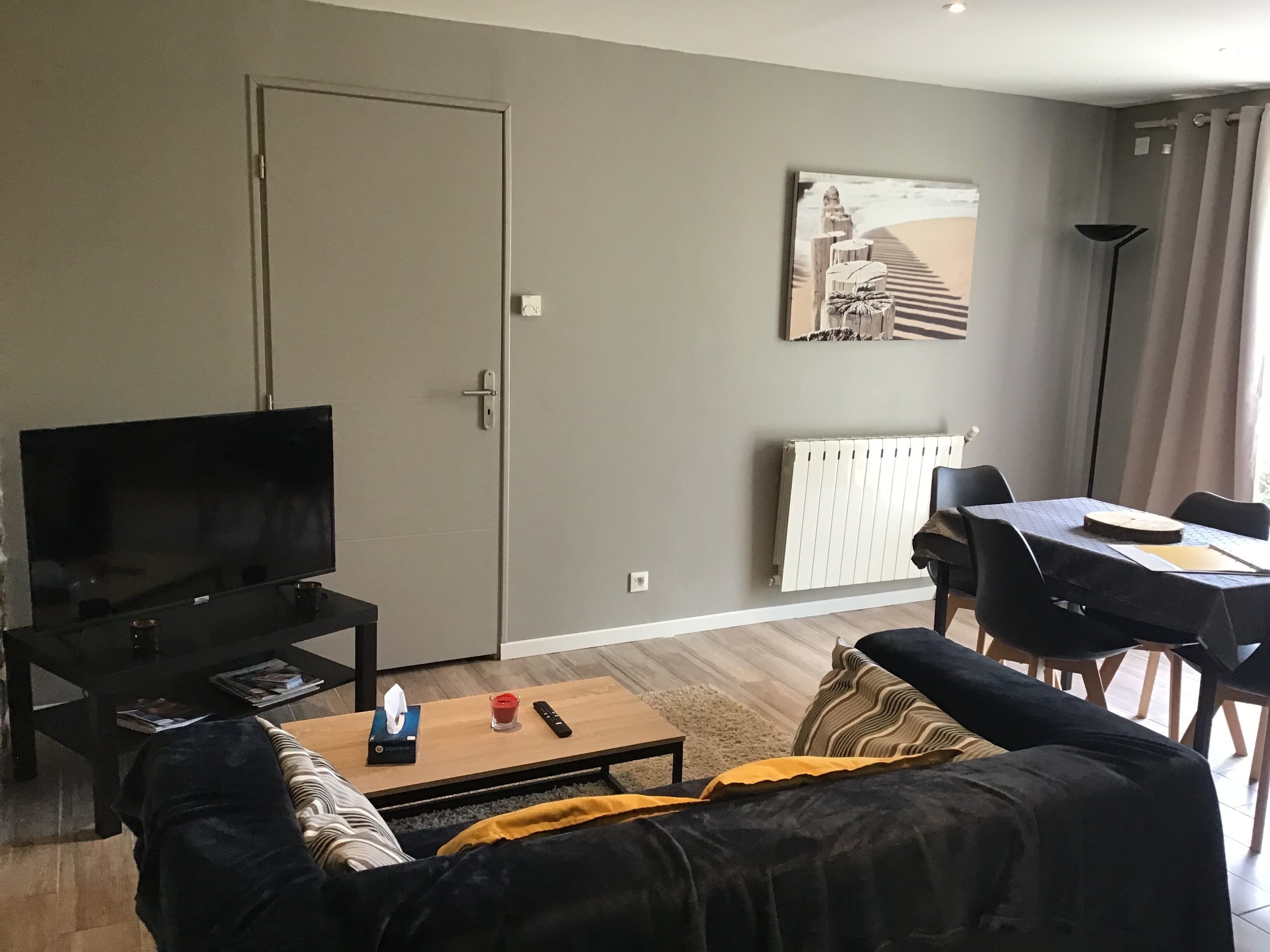A living room with a flat-screen TV, a coffee table, a sofa, and a dining area with a table and chairs.