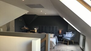 Ein modernes Schlafzimmer im Loft-Stil mit schrägem Dach, einem Bett, einem Sessel und einem kleinen Tisch.