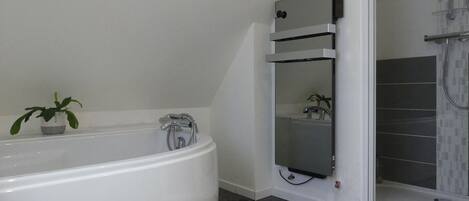 A modern bathroom with a freestanding bathtub, a small potted plant, and a shower area with a glass door.