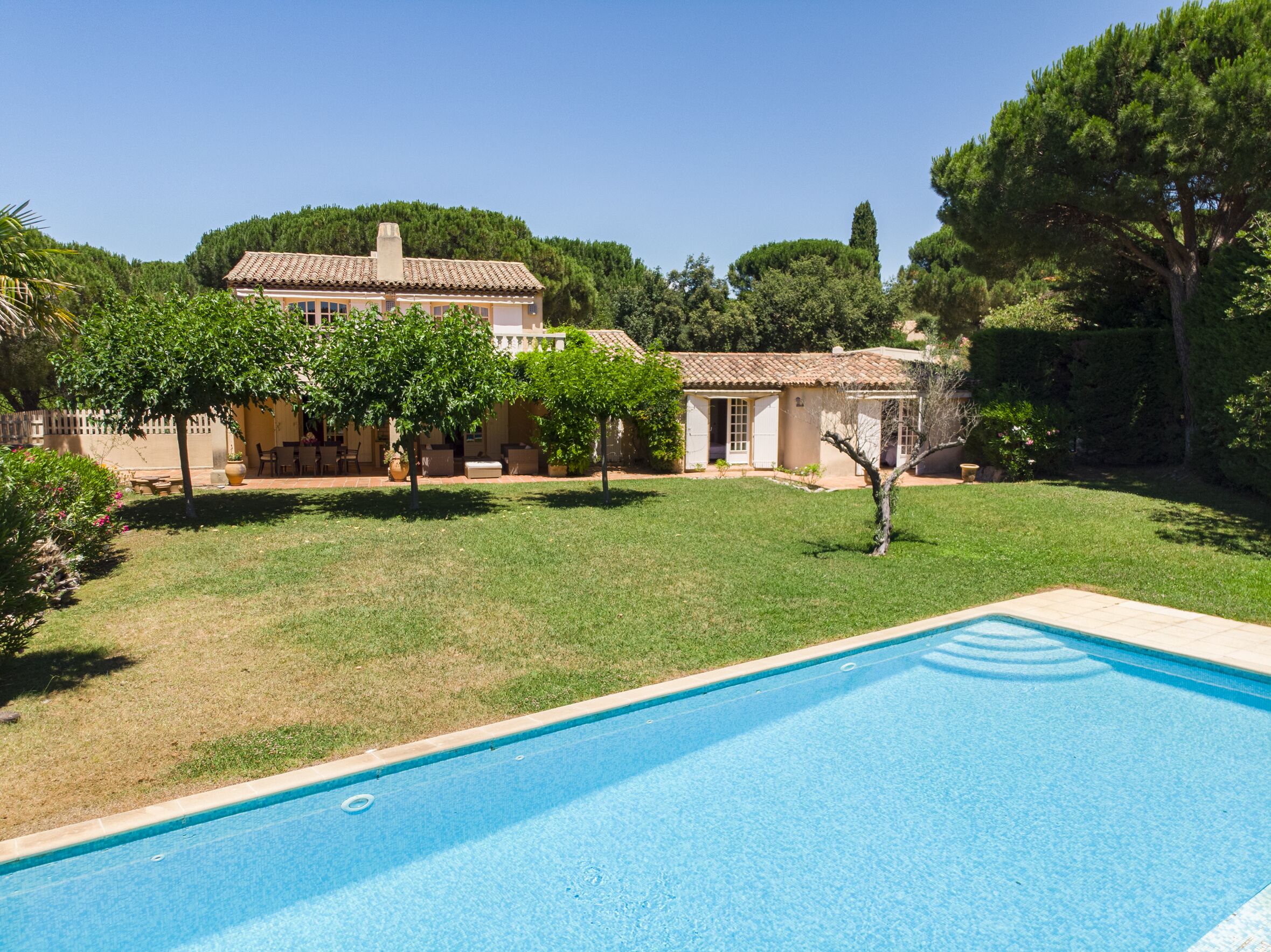 A swimming pool with a tiled deck, surrounded by a well-maintained lawn and a house with a tiled roof.