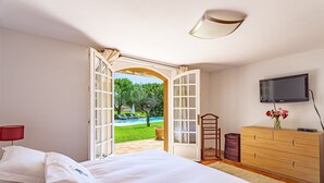 Ein Schlafzimmer mit einem Bett, einer Kommode, einem Fernseher und einer offenen Tür zu einem Poolbereich.