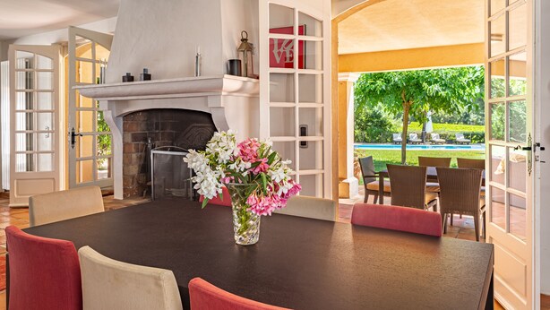 Ein Essbereich mit Kamin, einem Blumenstrauß und Blick auf Pool und Garten.