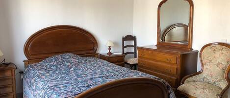 Un dormitorio con una cama de madera, un aparador, una silla y un espejo.