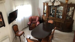 A dining area with a round table and six chairs, a television mounted on the wall, and a cabinet with glass doors.
