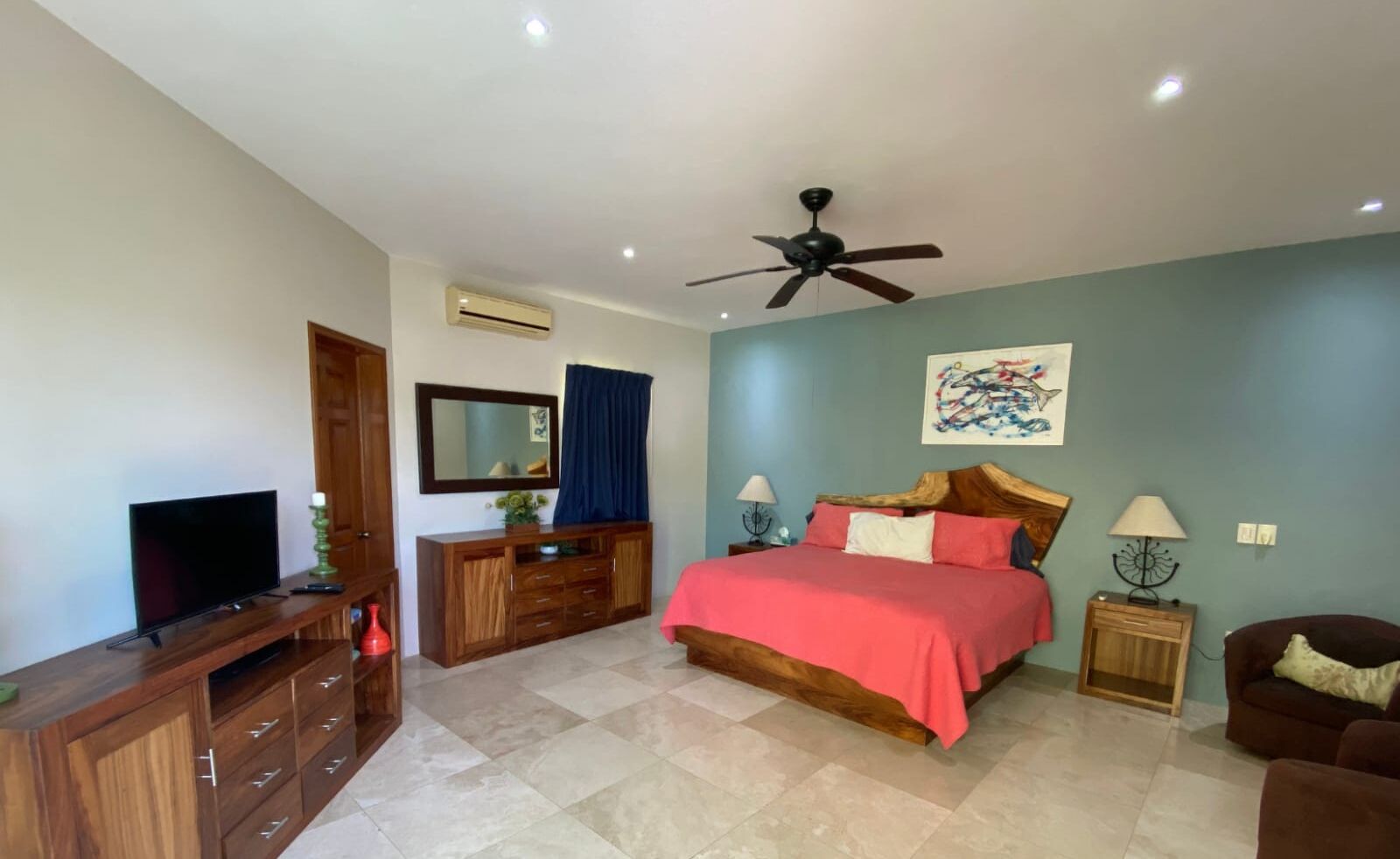 Un dormitorio con cama, televisor, ventilador de techo, cómoda y un cuadro en la pared.