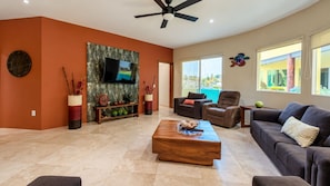 A spacious living room with a flat-screen TV, comfortable seating, a coffee table, and a large window with a view.
