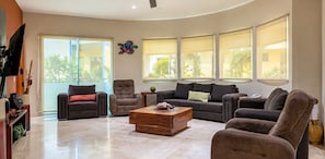 A modern living room with a sofa, armchairs, a coffee table, and large windows with blinds.