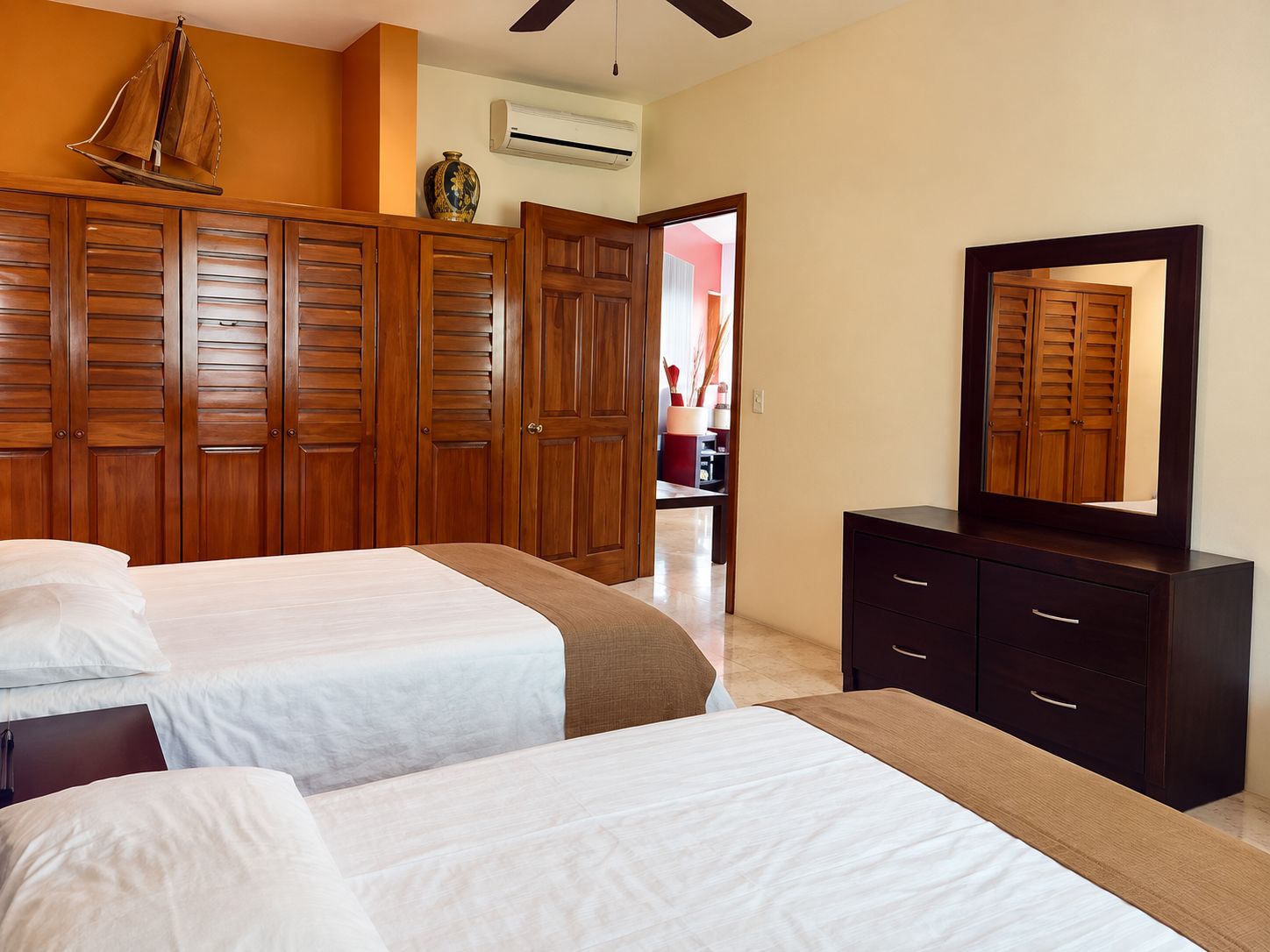 A hotel room with two beds, wooden wardrobes, a dresser, and a ceiling fan.