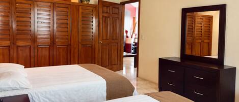 A hotel room with two beds, wooden wardrobes, a dresser, and a ceiling fan.