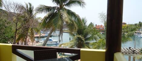 A balcony with a table and chairs, overlooking a marina with boats and palm trees.