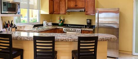 A kitchen with a central island, wooden cabinets, stainless steel appliances, and a window providing natural light.