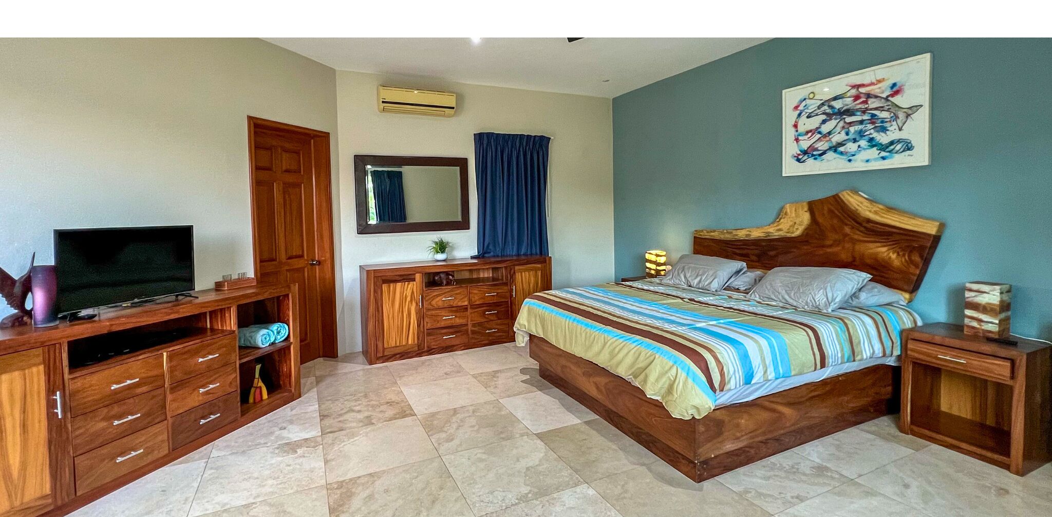Een slaapkamer met een bed, een houten dressoir, een televisie en een schilderij aan de muur.