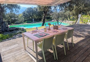 Ein Essbereich im Freien mit einem Tisch für vier Personen, mit Blick auf einen Swimmingpool und die natürliche Landschaft.