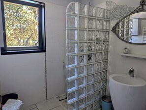 Ein Badezimmer mit Duschkabine aus Glas, einem Fenster, einem Waschbecken und einem Spiegel.