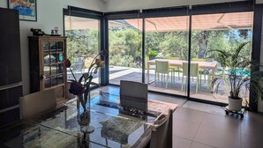 A modern kitchen with a glass dining table, a cabinet, and a view of the outdoor patio. - Villa in Lumio, large swimming pool, wooded park   (Lumio)