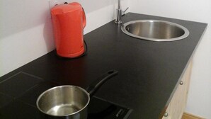 A compact kitchen with a black countertop, a stainless steel sink, a red kettle, and a pot on an induction cooktop. - Studio with a View of Mont Blanc in Sallanches (Sallanches)