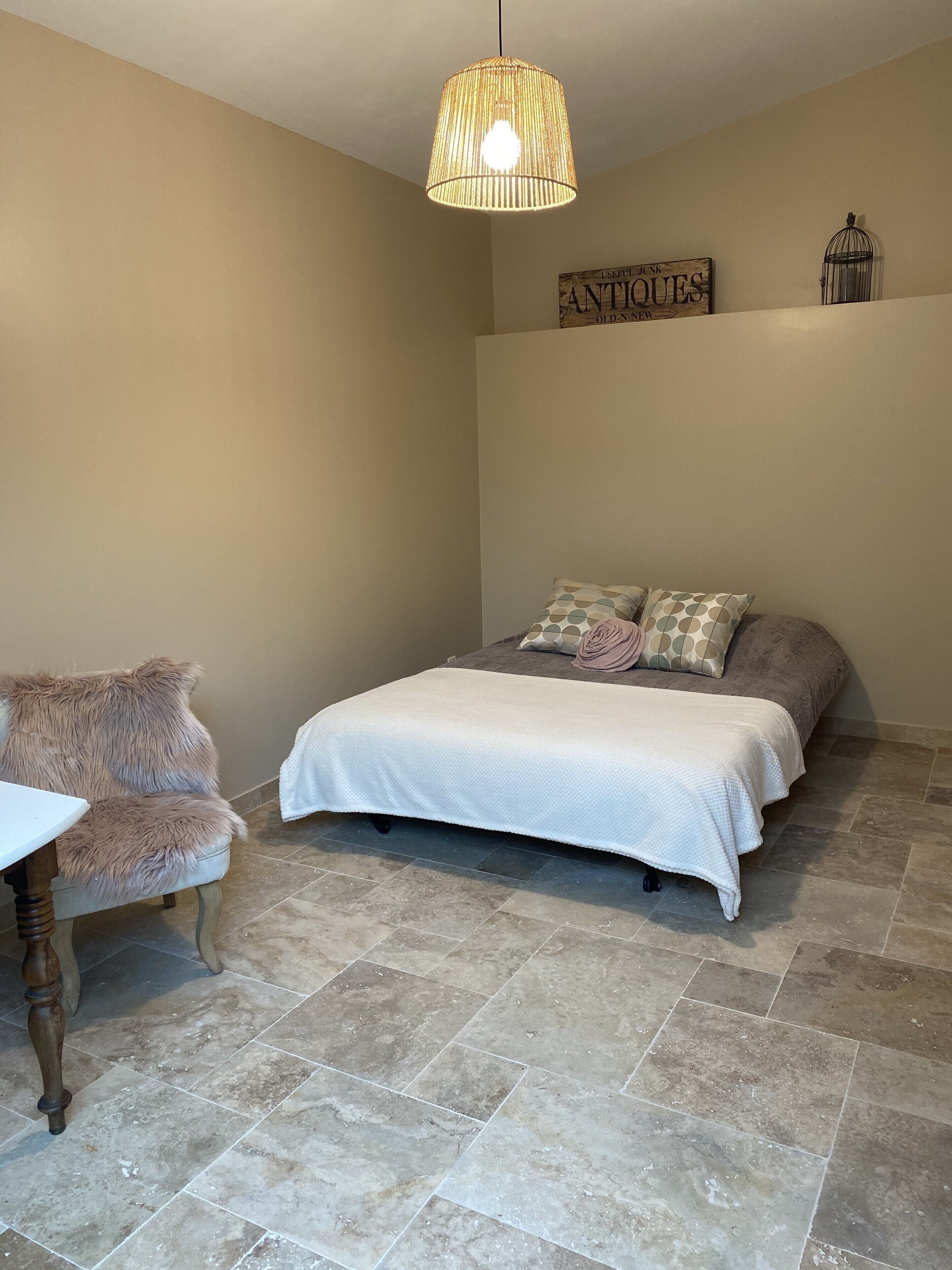 A bedroom with a bed, a chair, a hanging light fixture, and a wall sign.