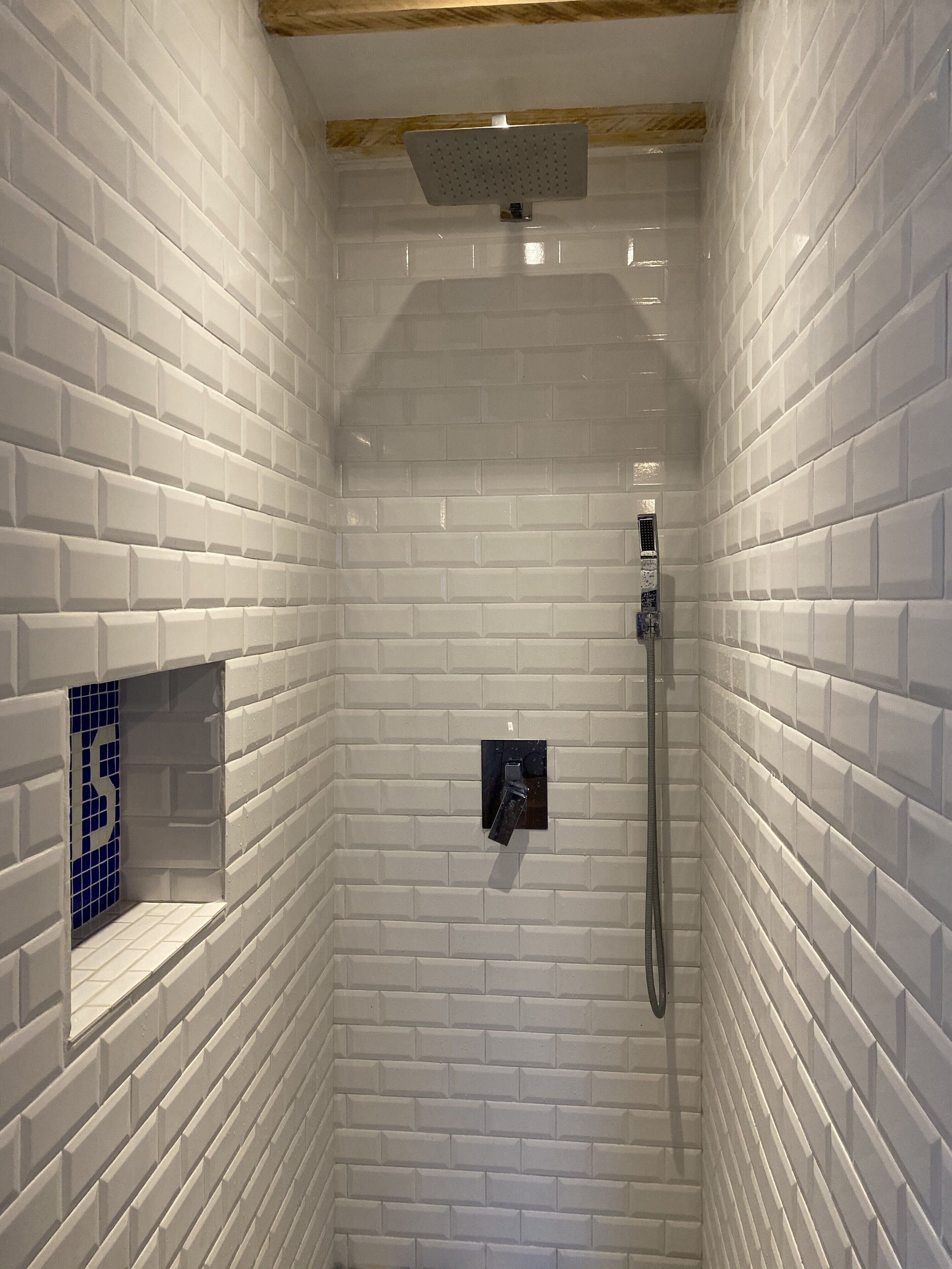 Un angolo doccia con pareti piastrellate di bianco e soffitto in legno.