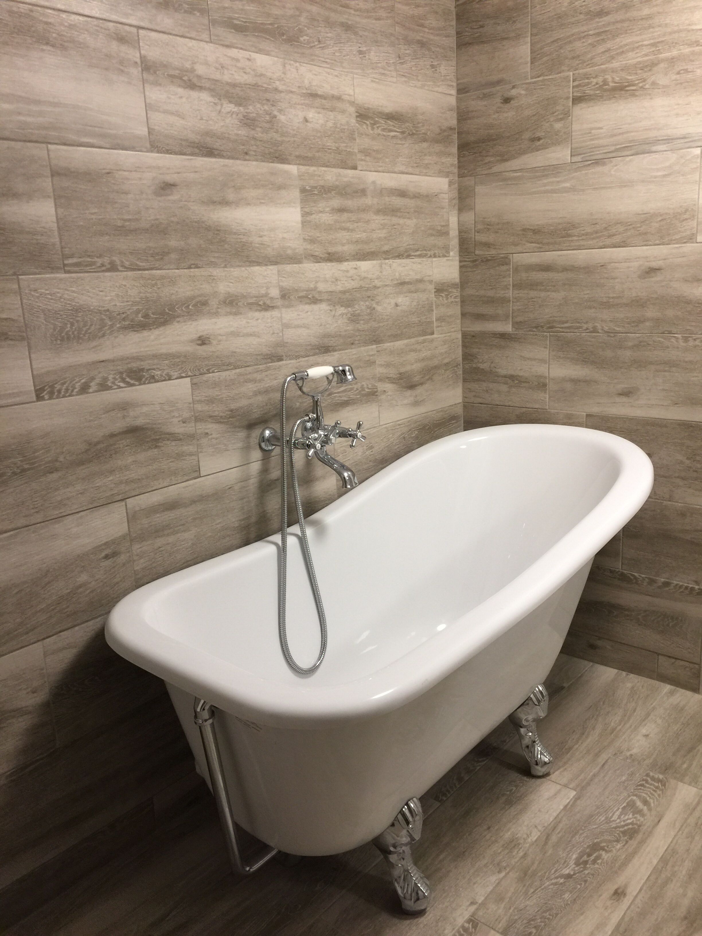 Une baignoire sur pieds dans une salle de bain avec un plancher en bois et des murs carrelés.