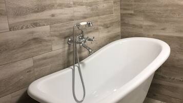 Une baignoire sur pieds dans une salle de bain avec un plancher en bois et des murs carrelés.