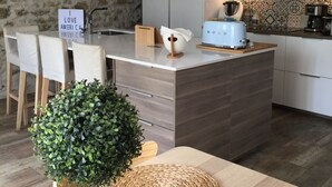 A modern kitchen with a central island, a stone wall, and a dining area with a table and chairs.