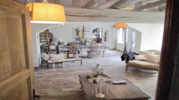 A rustic interior with exposed wooden beams, a dining area with a table and chairs, and a cozy seating area with a sofa and a decorative birdcage.