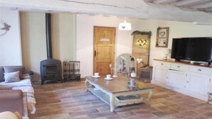 A cozy living room with a fireplace, a dining table set with cups and saucers, a television, and a kitchen area.