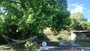 A stone wall, a hammock, a pool, and a Buddha statue in a garden.
