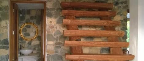 A wooden staircase with a stone wall on one side and a wooden door leading to a bathroom.