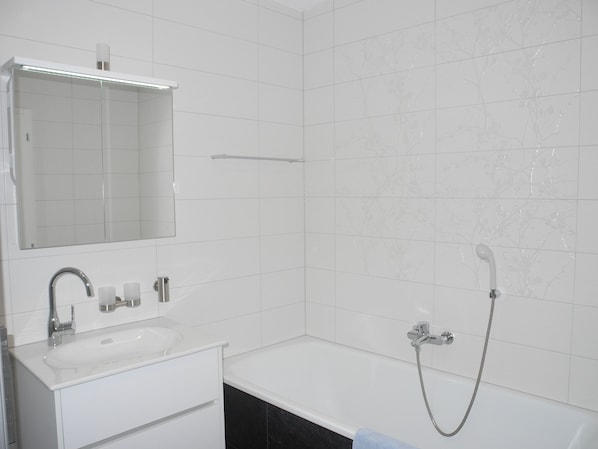 A modern bathroom with a white sink, mirror, and bathtub. - Modern, new 3.5-room apartment in brig with fantastic views of the mountains (Brig-Glis)