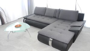 A modern living room with a grey sectional sofa, a glass coffee table, and a grey ottoman. - Modern, new 3.5-room apartment in brig with fantastic views of the mountains (Brig-Glis)