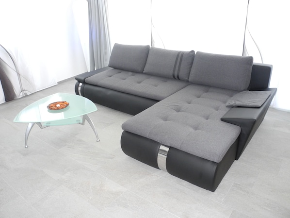 A modern living room with a grey sectional sofa, a glass coffee table, and a grey ottoman.