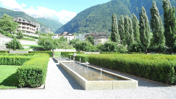 A landscaped garden with a rectangular water feature, neatly trimmed hedges, and a pathway. - Modern, new 3.5-room apartment in brig with fantastic views of the mountains (Brig-Glis)