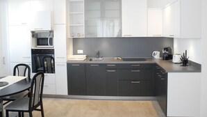 A modern kitchen with white cabinets, a black countertop, and a built-in oven. - Modern, new 3.5-room apartment in brig with fantastic views of the mountains (Brig-Glis)
